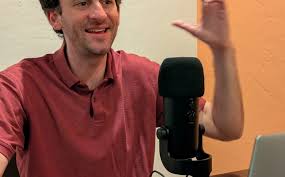 A man excitedly lifts his hands in front of a podcast mic